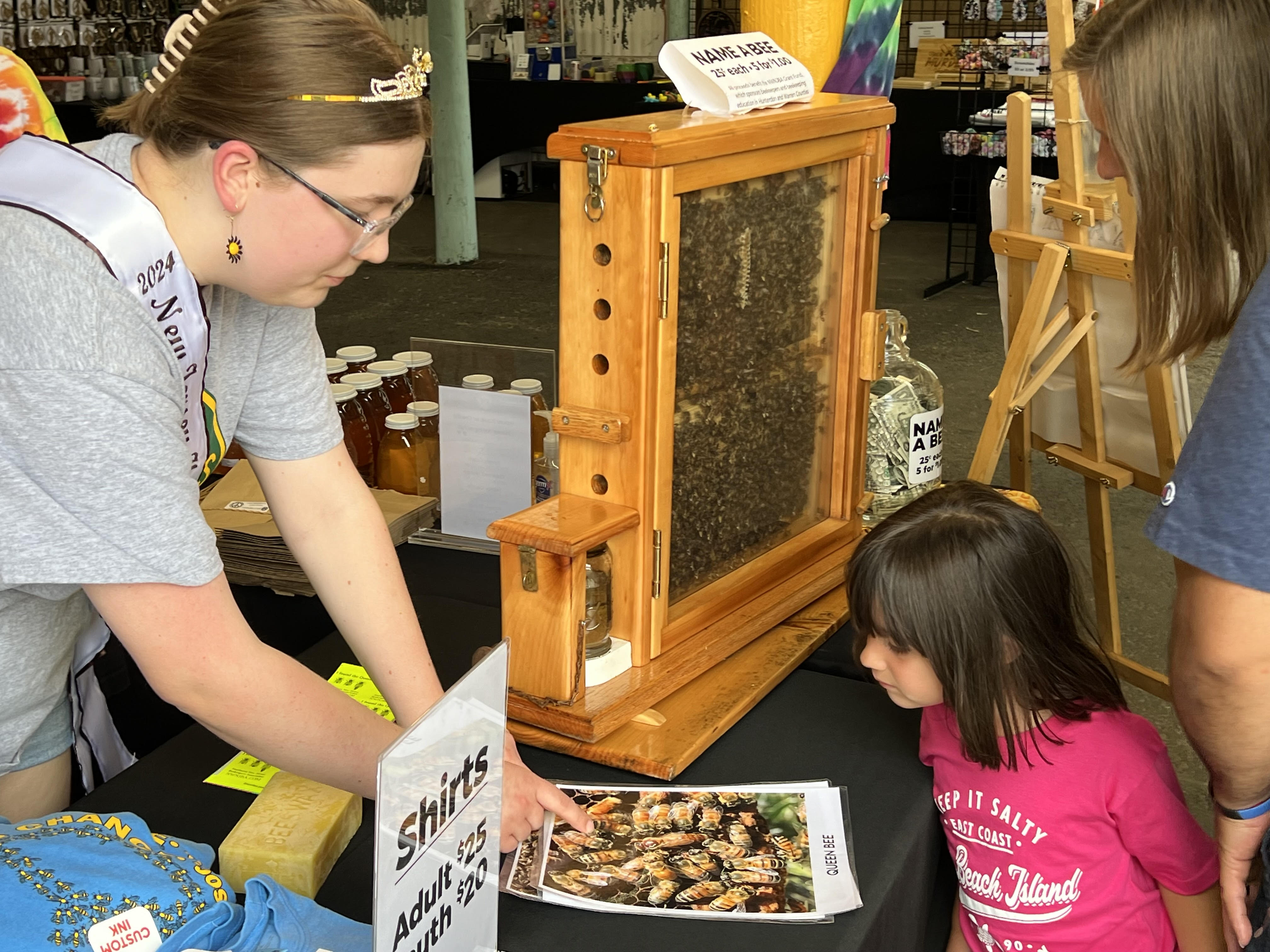 2024 NJ Honey Queen, Maddie Tubbs showing the queen bee to an interested young onlooker.